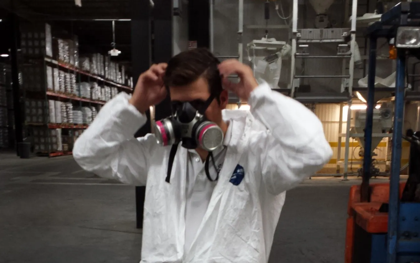 A Marrone technician pulling on his respirator inside a processing plant, racking and a bagging line behind him