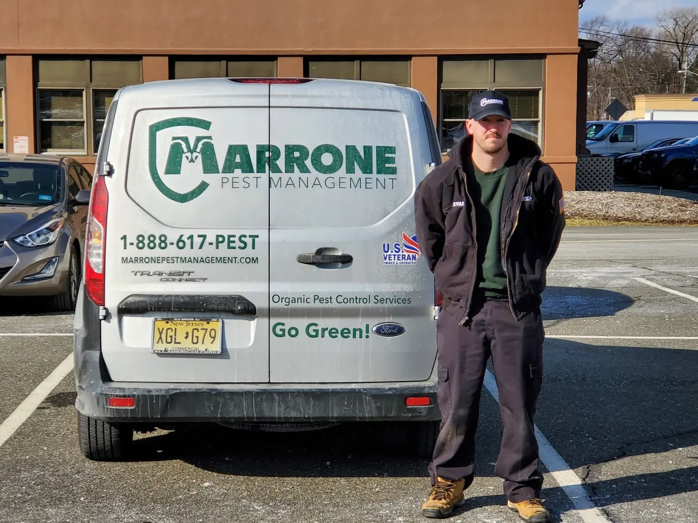 A Marrone Pest Management technician standing beside the rear of a company van, its logo, 1-888-617-PEST number and US Veteran Owned badge in view