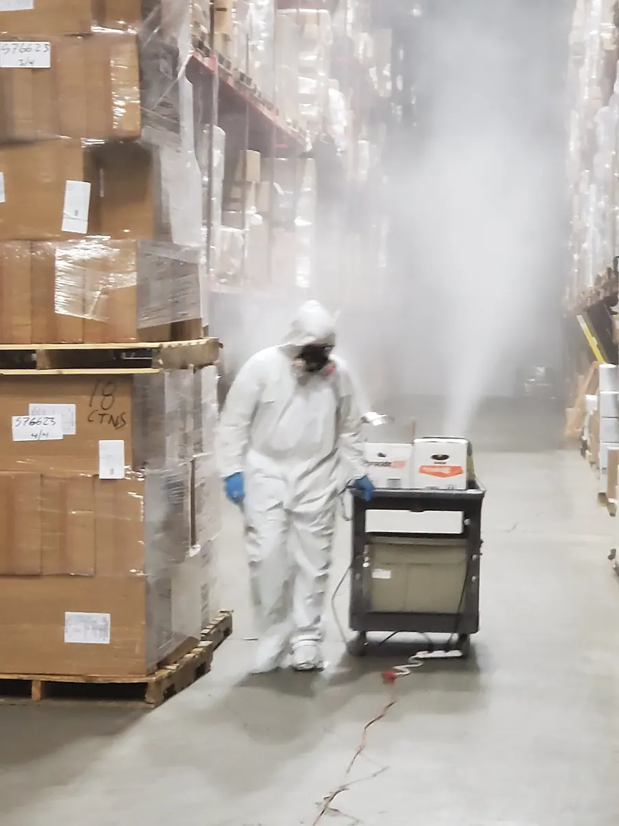 A Marrone technician in a protective suit and respirator fogging a warehouse